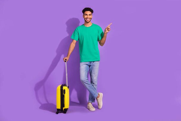 Full length photo of young satisfied traveler guy stay with baggage direct finger empty space new country isolated on violet color background. - Foto, Imagem