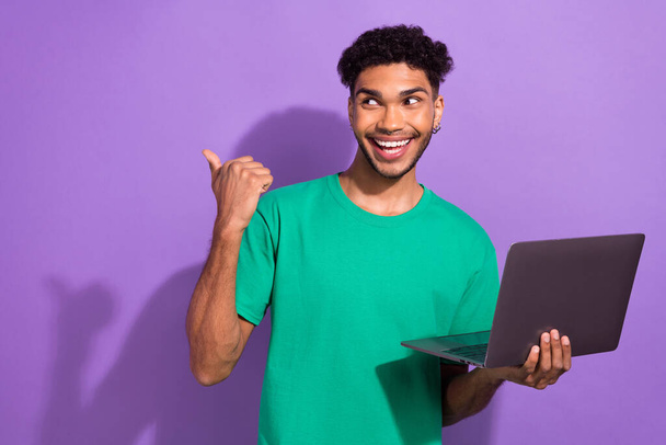 Photo of handsome cheerful guy hold netbook look indicate finger empty space promo isolated on violet color background. - Valokuva, kuva