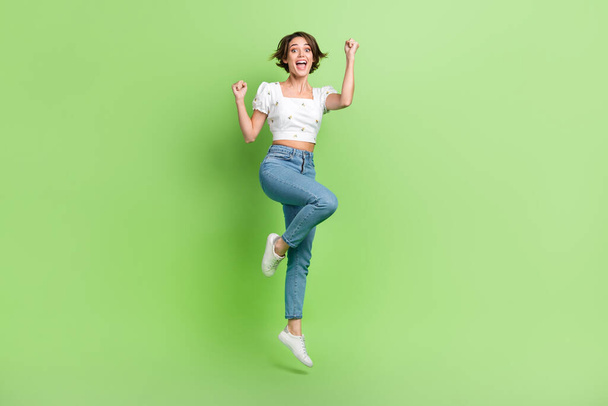 Full length photo of delighted carefree person jumping raise fists empty space isolated on green color background. - Zdjęcie, obraz