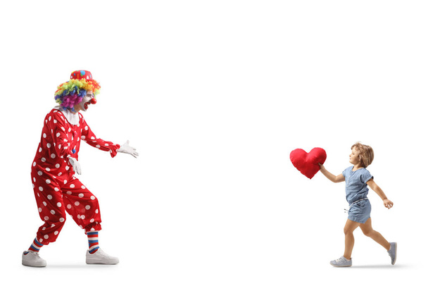 Full length shot of a little girl carrying a heart and running to hug a clown isolated on white background - Foto, Bild