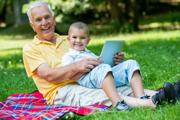 Grandfather and child in park using tablet - 写真・画像