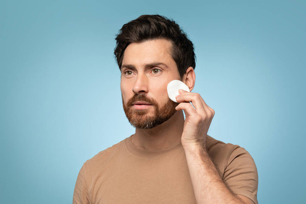 Refreshing rejuvenation. Males daily skincare routine with toner and cotton pads, middle aged man cleaning face skin over blue studio background, free space - Foto, Imagem