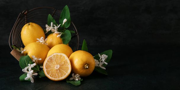 Overturned basket with lemons and blooming branches on black background with space for text - Фото, изображение