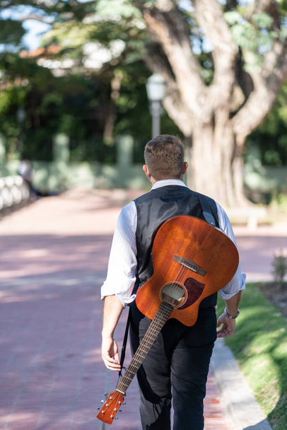 Vue arrière d'un guitariste marchant, portant sa guitare pendue sur son dos - Photo, image
