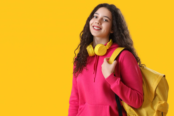 Studentessa con cuffie e zaino su sfondo giallo - Foto, immagini