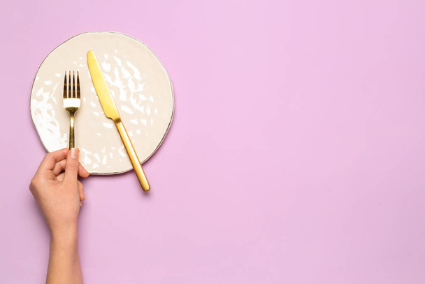 Mano femenina con plato vacío y cubiertos sobre fondo lila - Foto, imagen