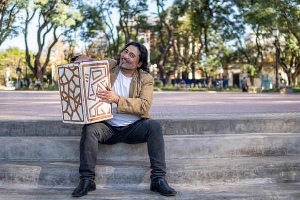 公園で彼のフラメンコボックスを抱いているヒスパニック系のミュージシャン - 写真・画像