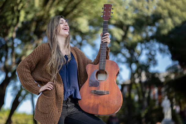 Mujer rubia joven con su guitarra en el parque. Concepto de afición creativa y profesionales. Actitud positiva. Empoderamiento. - Foto, imagen