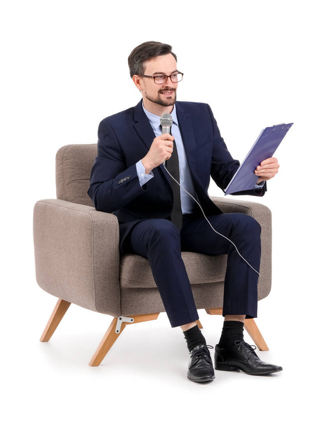 Jornalista masculino com microfone e prancheta em poltrona sobre fundo branco - Foto, Imagem