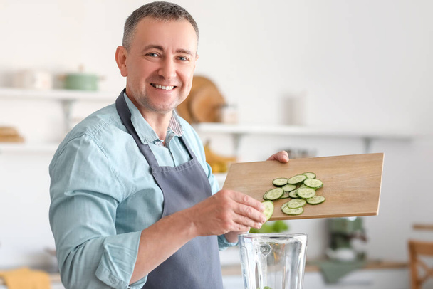 Reifer Mann legt Gurkenscheiben in Mixer in Küche - Foto, Bild