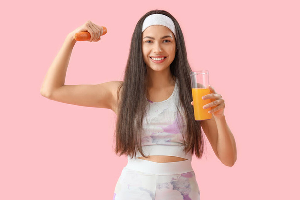 Sportliche junge Frau mit einem Glas Gemüsesaft und Karotte auf rosa Hintergrund - Foto, Bild