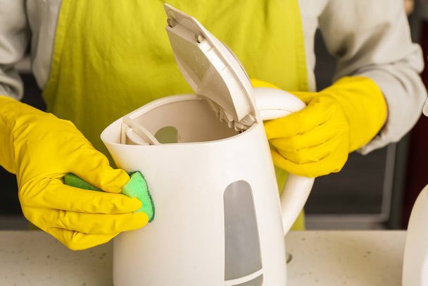 Frau in gelben Handschuhen putzt Wasserkocher auf weißem Tisch - Foto, Bild