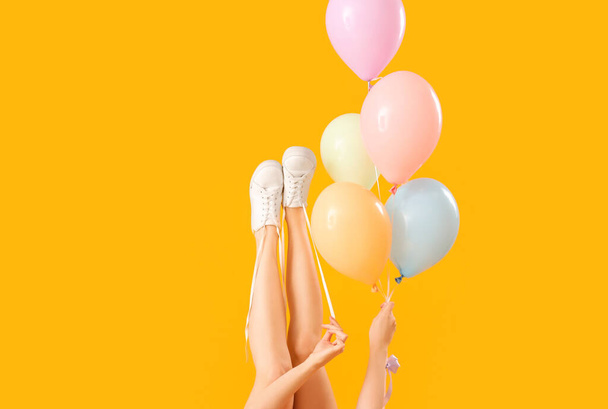 Young woman tying shoes laces with balloons on yellow background - Foto, Bild