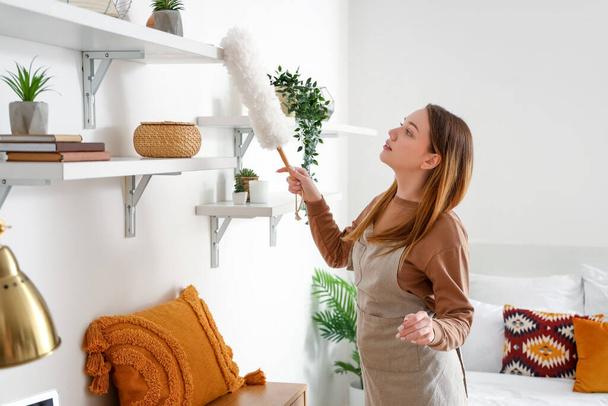 Mujer joven limpiando estante con pp-duster en el dormitorio - Foto, imagen