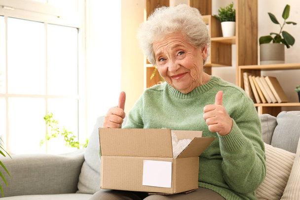 Mujer mayor con paquete abierto mostrando pulgares hacia arriba en casa - Foto, imagen