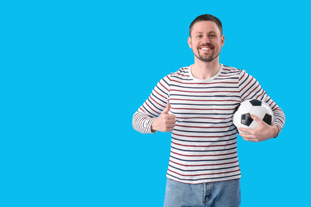 Uomo con pallone da calcio che mostra pollice in su su su sfondo blu - Foto, immagini
