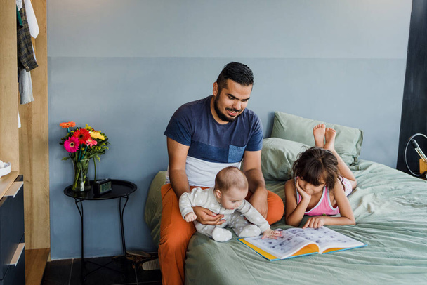 young latin single father with baby son and daughter on bed at home in Mexico Latin America, hispanic family - Valokuva, kuva