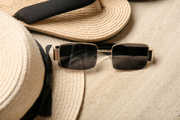 Κομψά γυαλιά ηλίου με καπέλο και σαγιονάρες στην άμμο - Φωτογραφία, εικόνα