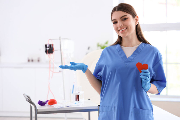 Infirmière avec coeur en papier montrant quelque chose en clinique - Photo, image