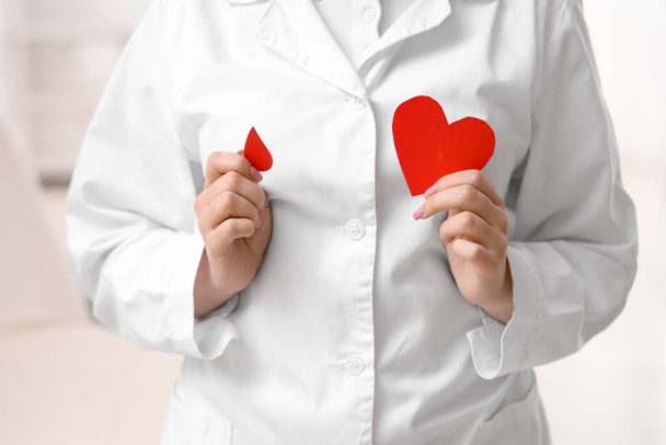 Female doctor with paper blood drop and heart in clinic, closeup - Photo, Image