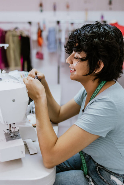 Latin kökenli genç bir kadın moda tasarımcısı Meksika 'daki atölyesinde dikiş makinesiyle çalışıyor. Latin Amerika' da, Latin kökenli küçük işletme sahibi kadın. - Fotoğraf, Görsel