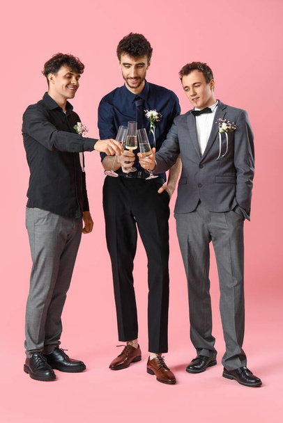 Young men dressed for prom with glasses of champagne on pink background - Foto, imagen