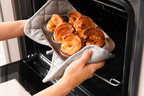 Frau holt Backform mit leckerem Yorkshirepudding aus Ofen in Küche - Foto, Bild
