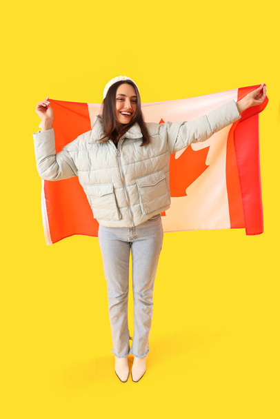 Sarı arka planda Kanada bayrağı olan sıcak şapkalı genç bir kadın. - Fotoğraf, Görsel