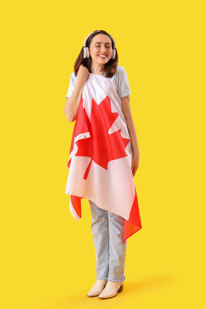 Νεαρή γυναίκα με ακουστικά με σημαία Καναδά σε κίτρινο φόντο - Φωτογραφία, εικόνα