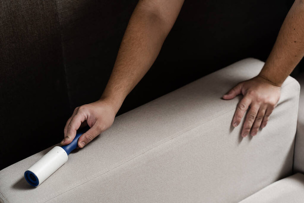 Process of cleaning couch using lint roller from cat and dog hair. Cleaner is removing lint from sofa using cleaning roller close-up - Foto, Imagem