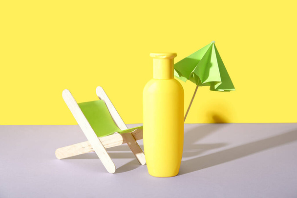Sarı duvarın yanındaki leylak masasında minyatür iskemle ve bir şişe güneş kremi bulunan yaratıcı bir kompozisyon. - Fotoğraf, Görsel