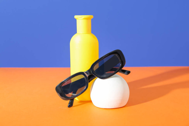 Bottle of sunscreen cream with sunglasses on orange table near blue wall - Foto, Imagen