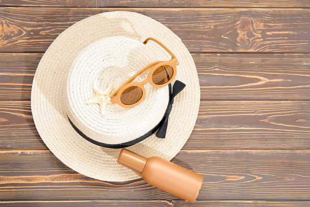 Bottle of sunscreen cream, sunglasses and wicker hat on wooden background - Foto, afbeelding