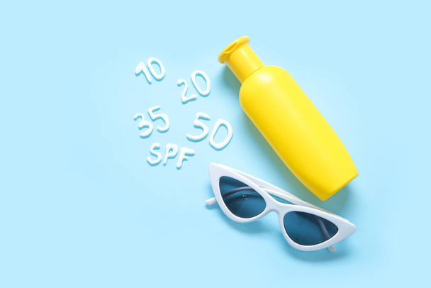 Palavra SPF com números feitos de creme protetor solar e óculos de sol em fundo azul - Foto, Imagem