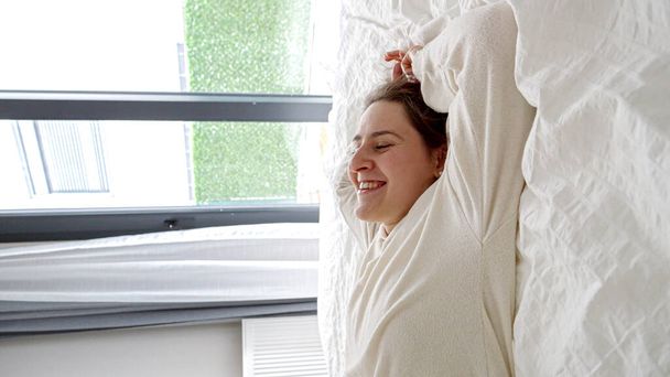 Lento movimiento de mujer alegre en pijama cayendo en la cama sobre su espalda. Concepto de felicidad, relajación en casa, comodidad, diversión en casa - Foto, imagen