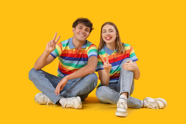 Giovane coppia in camicie arcobaleno che mostra il gesto della vittoria su sfondo giallo - Foto, immagini