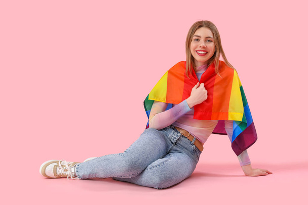 Giovane donna con bandiera LGBT seduta su sfondo rosa - Foto, immagini