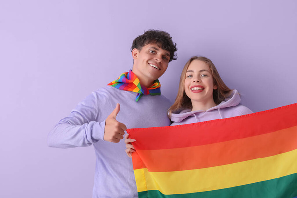 Young couple with LGBT flag on lilac background - Foto, afbeelding