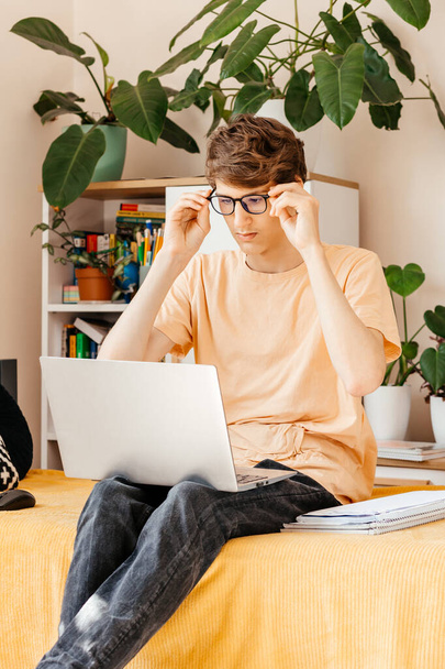 Jeune adolescent concentré travaillant sur un ordinateur portable sur le canapé à la maison. Smiled Boy fait ses devoirs avec un ordinateur. Distance, éducation en ligne pour les enfants - Photo, image