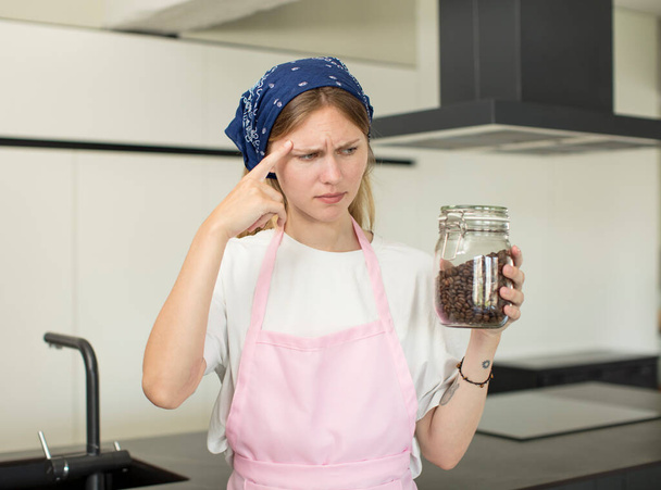 young pretty woman looking surprised, realizing a new thought, idea or concept. home chef with coffee beans - Foto, Imagen