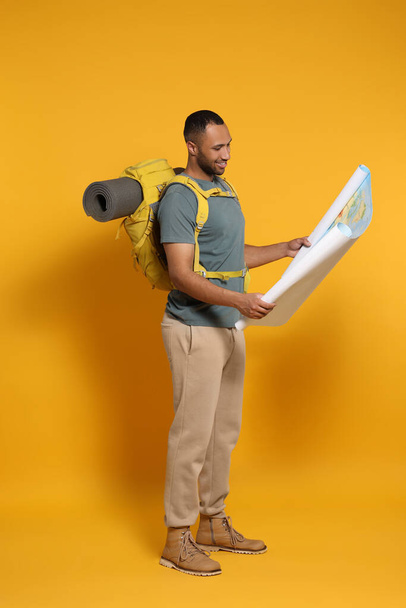 Happy tourist with backpack and map on yellow background - Foto, Bild