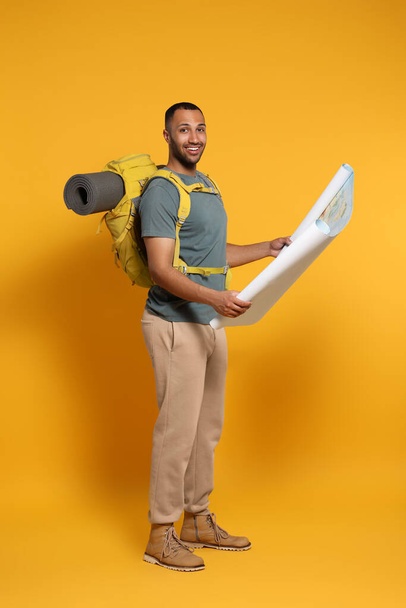 Happy tourist with backpack and map on yellow background - Foto, Imagen