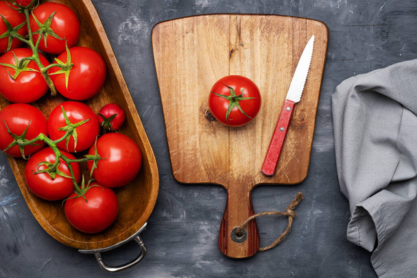 tuoreet, kypsät tomaatit puuastiassa ja leikkuulauta veitsellä harmaalla pohjalla. Näkymä ylhäältä. Tekstitila. - Valokuva, kuva