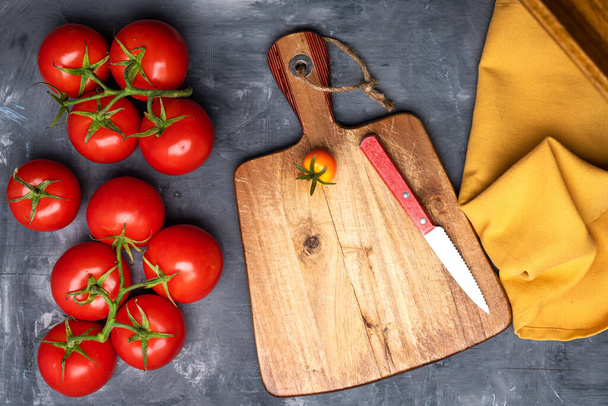 bunch of fresh, ripe tomatoes and a cutting board on a gray background. View from above. Space for text. - Foto, immagini