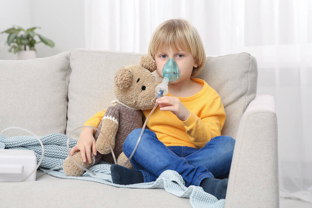 Boy with toy bear using nebulizer for inhalation at home - Foto, imagen
