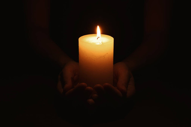 Woman holding burning candle in hands on black background, closeup - Photo, Image