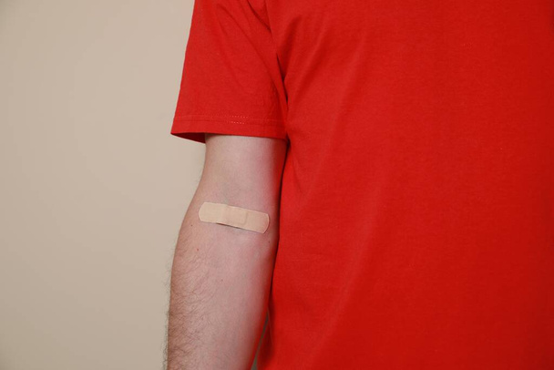 Blood donation concept. Man with adhesive plaster on arm against beige background, closeup - Foto, Imagem