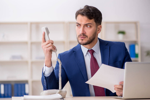 Jeune employé parlant par téléphone sur le lieu de travail - Photo, image