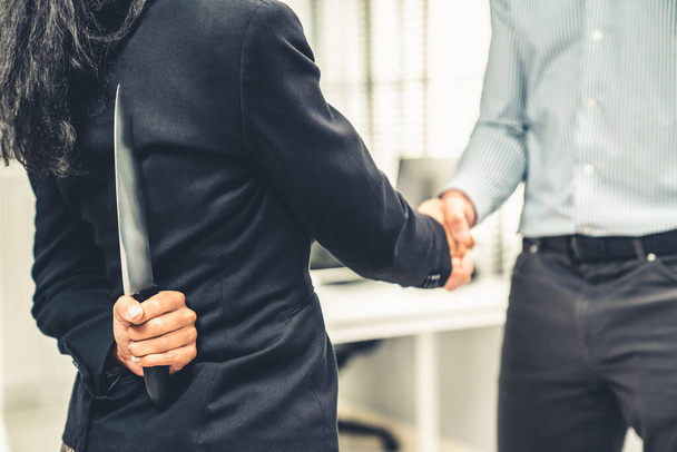 Back view of businesswoman shaking hands with another businessman while holding a knife behind his back. Concept of back backstabbing in business, backstabbing between colleagues. - Foto, afbeelding