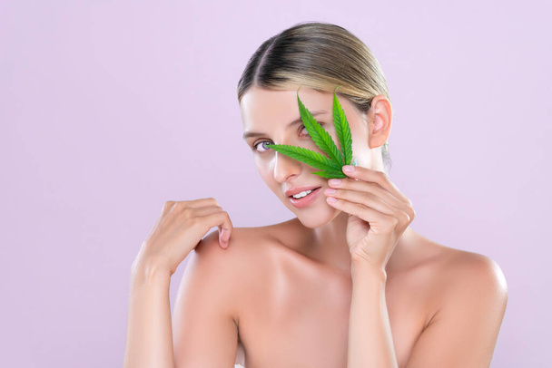 Portrait séduisant de belle femme modèle tenant la feuille verte comme concept pour le produit cosmétique de soins de la peau de cannabis pour un traitement de fraîcheur de peau parfait dans un fond rose isolé. - Photo, image